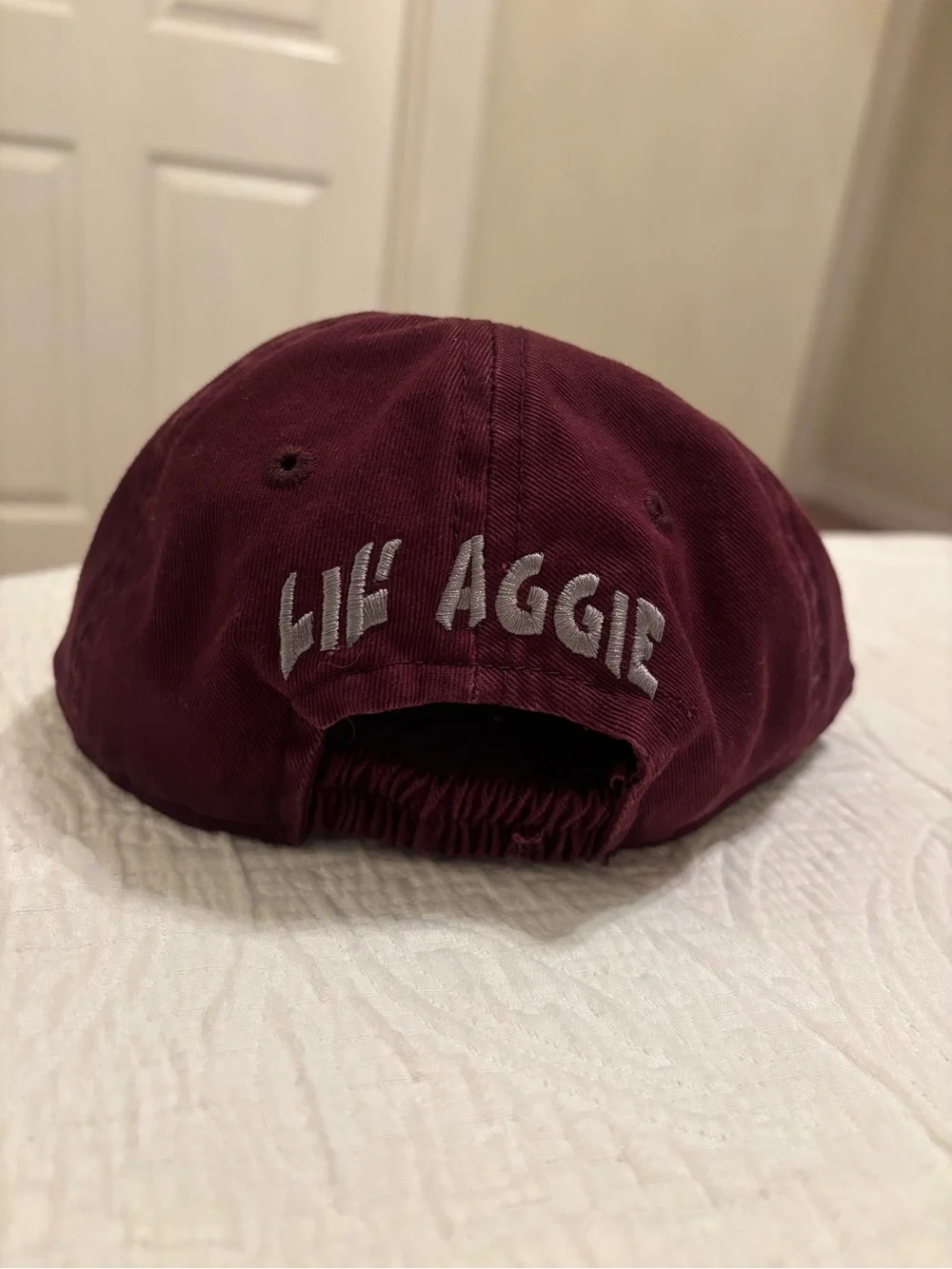 A&M baby baseball cap, elastic back w/ white embroidered A&M Logo & Lil’Aggie